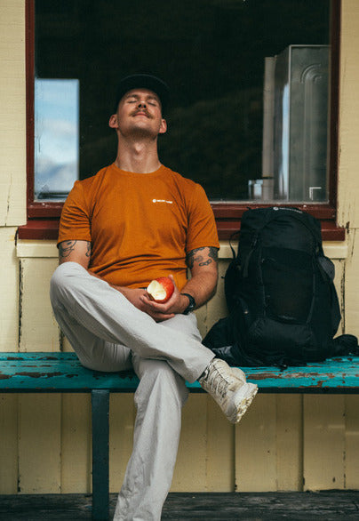 Man sat with eyes shut eating an apple alongside his rucksack