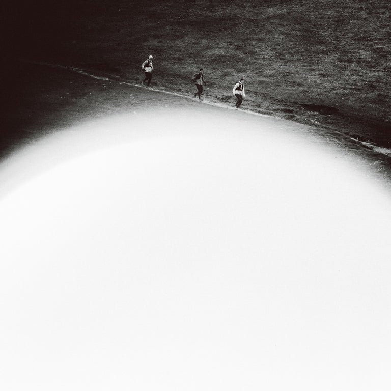 Black and white artistic photograph of three runners on the trail, dominated by a large bright white oval shape in the foreground.